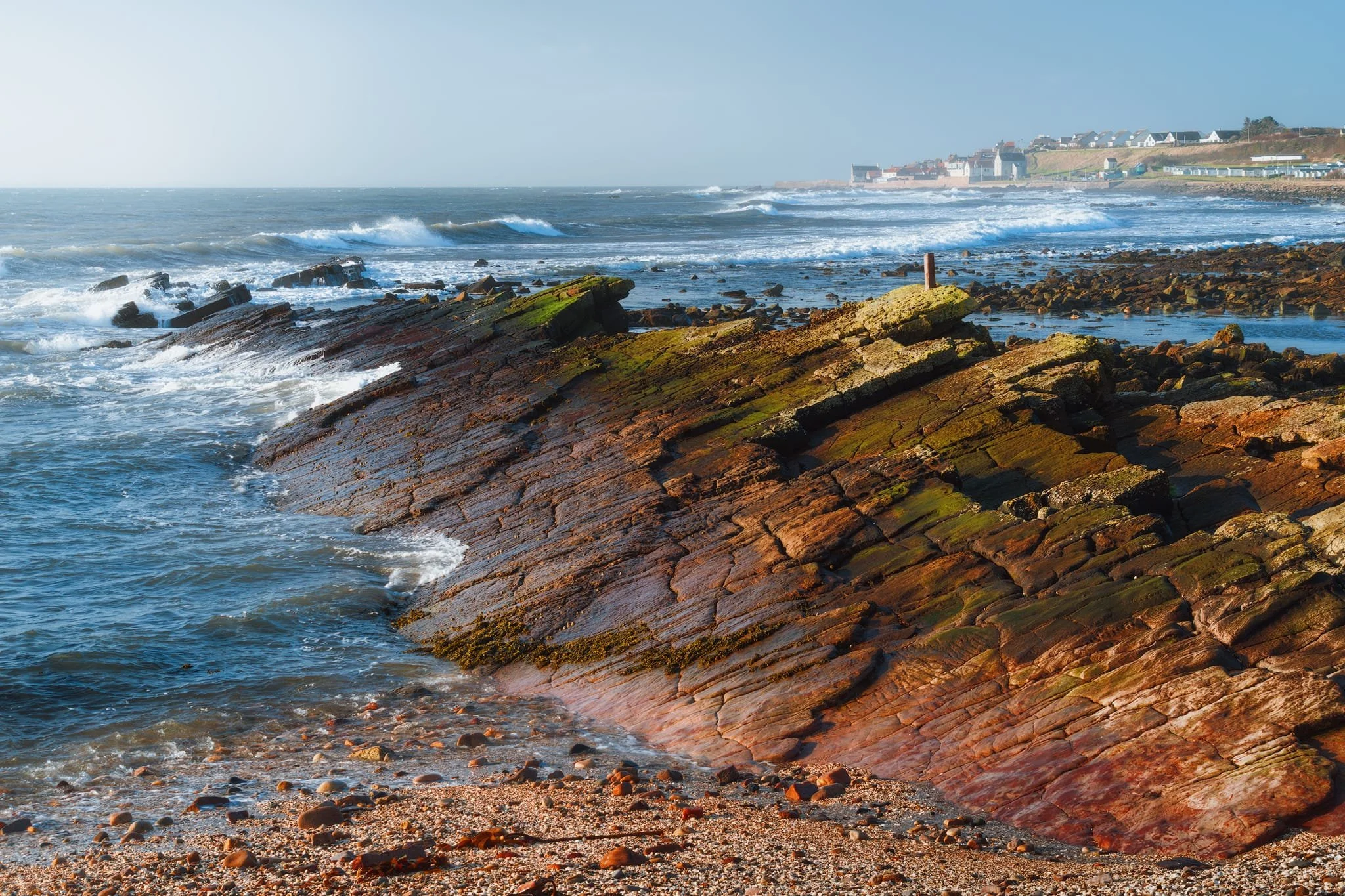 Standing back from these fascinating formations show them in context. A slightly hazy but clear day just about reveals Cellardyke in the background, whilst strong gusts push wave after wave into the coastline. A dramatic yet peaceful scene.