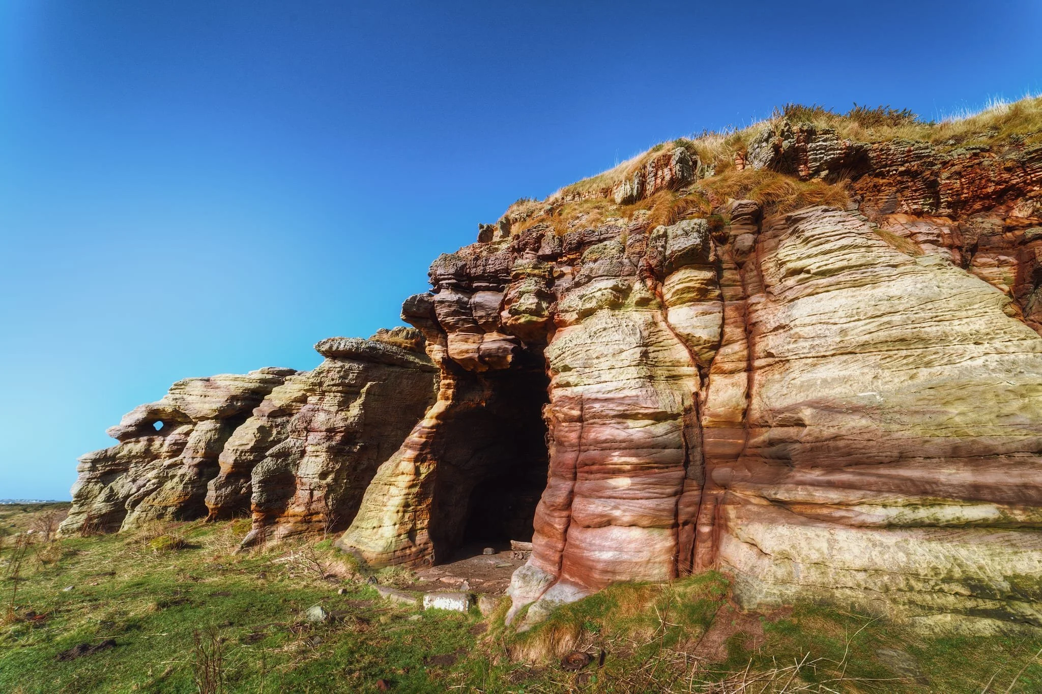 Roughly halfway between Anstruther and Crail this striking formation suddenly arrests your attention. These are the Caiplie Caves. They feature beautiful formations from around 370 to 360 million years ago. They’re notable for their bright stripes of pink, red, yellow, and cream colours, which show how the environment changed when the rocks were formed in ancient river systems and floodplains. The caves were shaped over time by the action of sea waves, which gradually wore away the softer rock layers while leaving the harder ones intact. This process created natural shelters along cracks in the rock, which were important as refuges for early Christian settlers in the coastal area of Fife. Isn’t it fascinating?