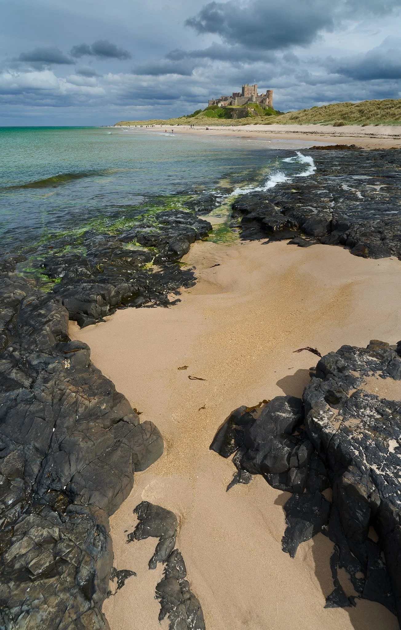  On Harkness Rocks, and the tide coming in, I picked out various compositions and watched the waves crash against the rocks, picking the aesthetically pleasing moments. In the distance, Bamburgh Castle is lit up by the dipping sun. 