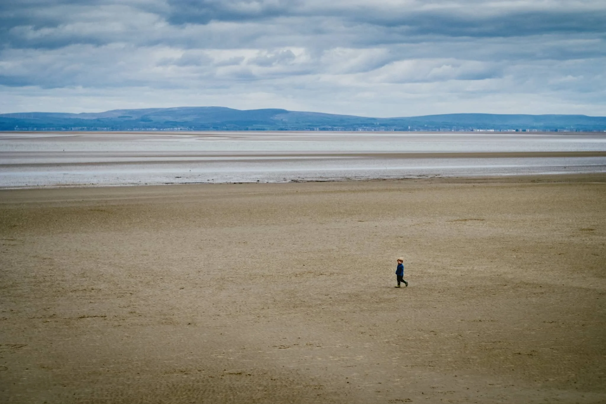 A small child, running freely across the sands of Bardsea beach.