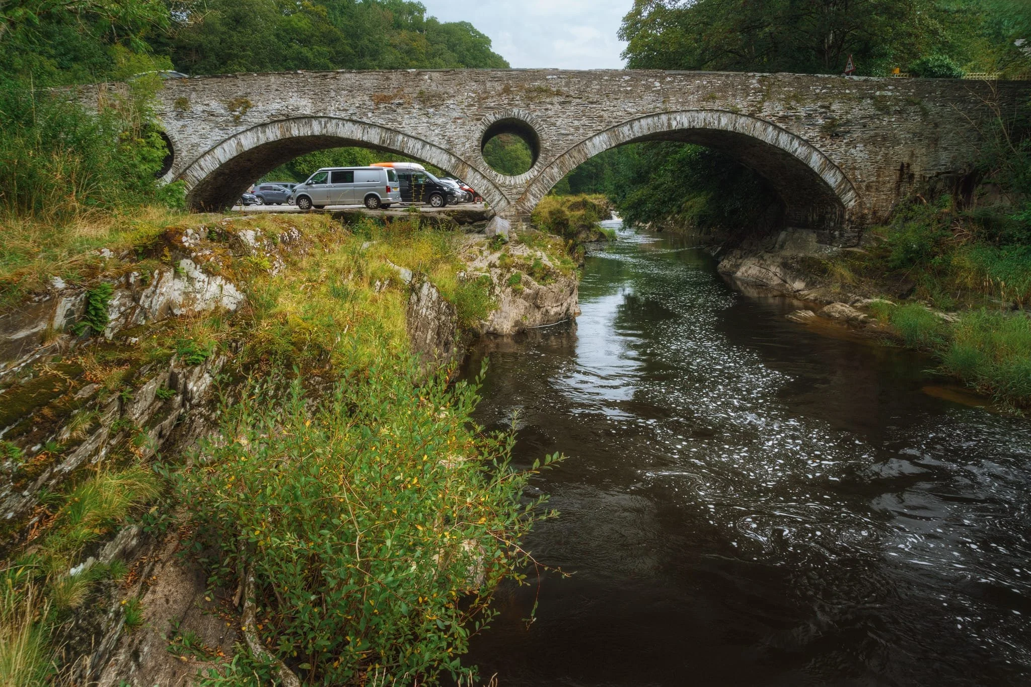  The beautiful Cenarth Bridge, unfortunately somewhat spoiled by all the parking that&rsquo;s allowed right next to it. It was built in the late 1700s. The holes, designed to reduce the structure&rsquo;s weight and allow floodwaters to pass through them, serve a crucial function. While the river typically flows only under the southern arch, during floods the  Teifi  surges through all three arches. 