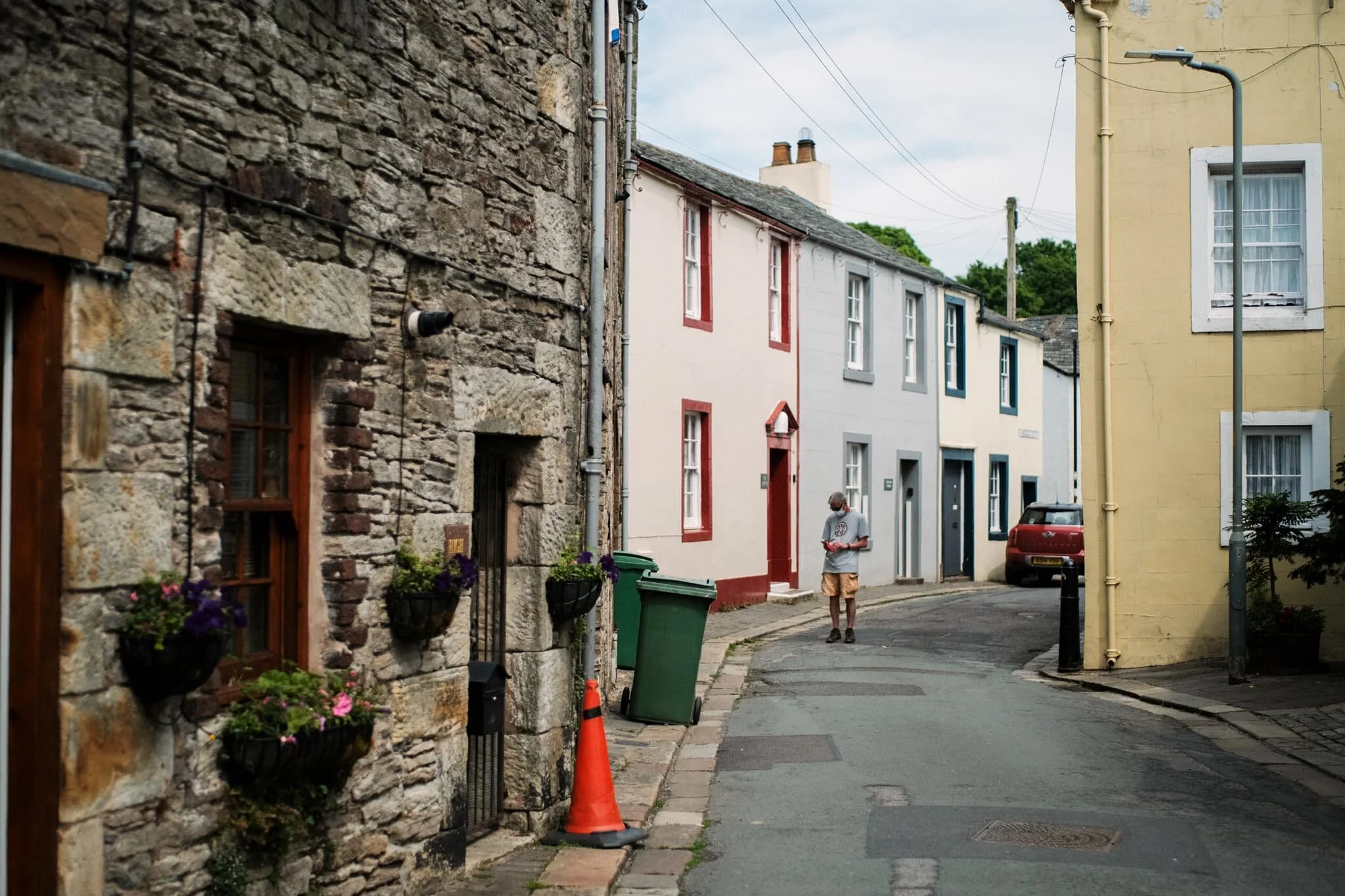 A partially-masked man pauses in the street to reply to someone on his phone.