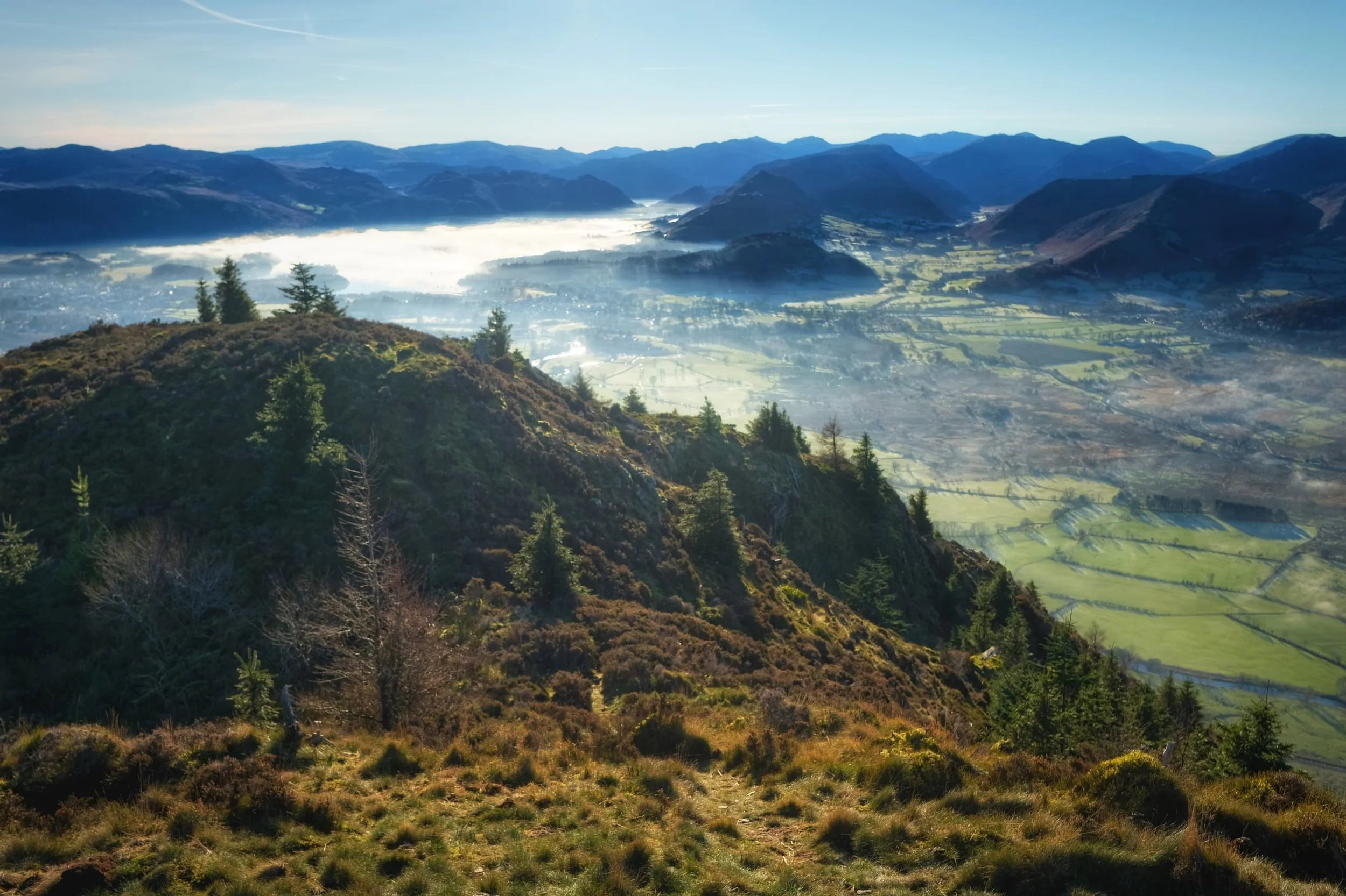  Nearing the summit of Dodd. To the left a temperature inversion clings to the surface of Derwentwater, creating a lake-sized mirror reflecting the morning sun. To the right are the Newland fells; tiny tufts of fog cling to dales below. 