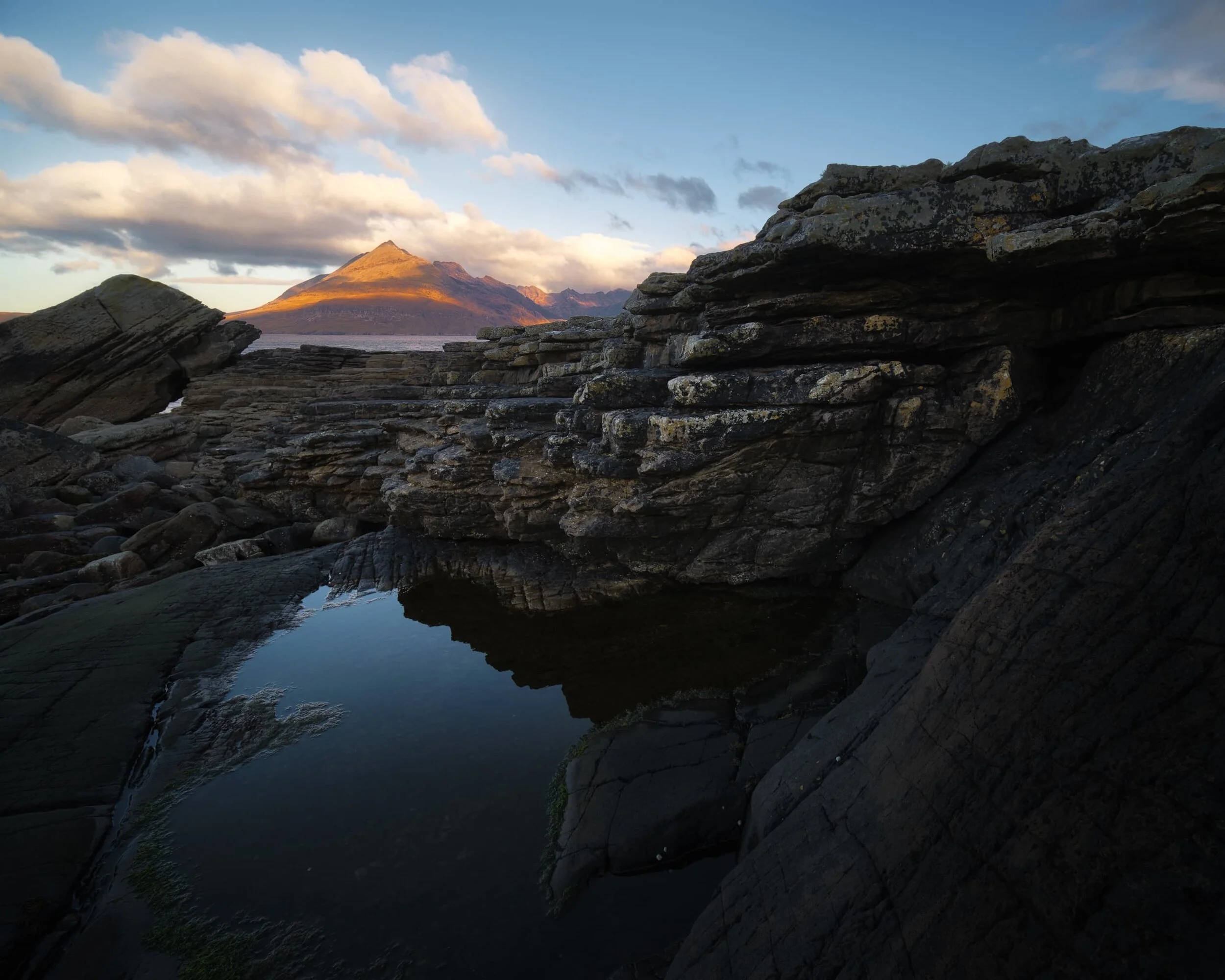  I immediately picked my way towards the northwestern shore, looking for compositions featuring some of Elgol&rsquo;s weird and wonderful rock formations. I found this stack of rock shelves, perhaps an  Uncomformity , which I used as a leading line towards the glowing Black Cuillins (the particular member of the Black Cuillins pictured is  Gars-bheinn , pronounced GAR-vein, meaning &ldquo;rough mountain&rdquo;). 