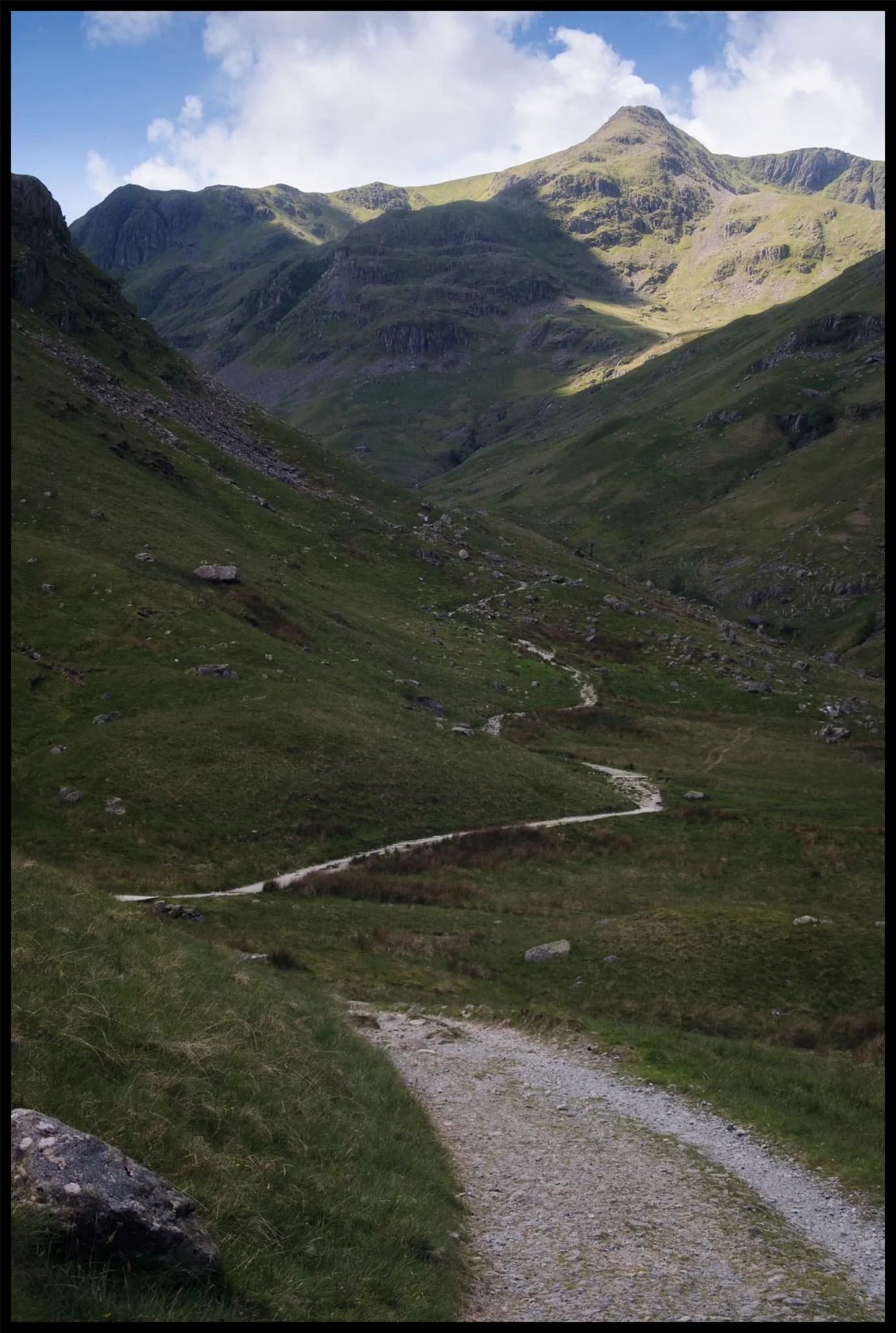  The path leads around the bottom of Post, on the left, a small crag that rise out of the valley floor. Above, Dollywaggon Pike is illuminated in between the racing clouds. 