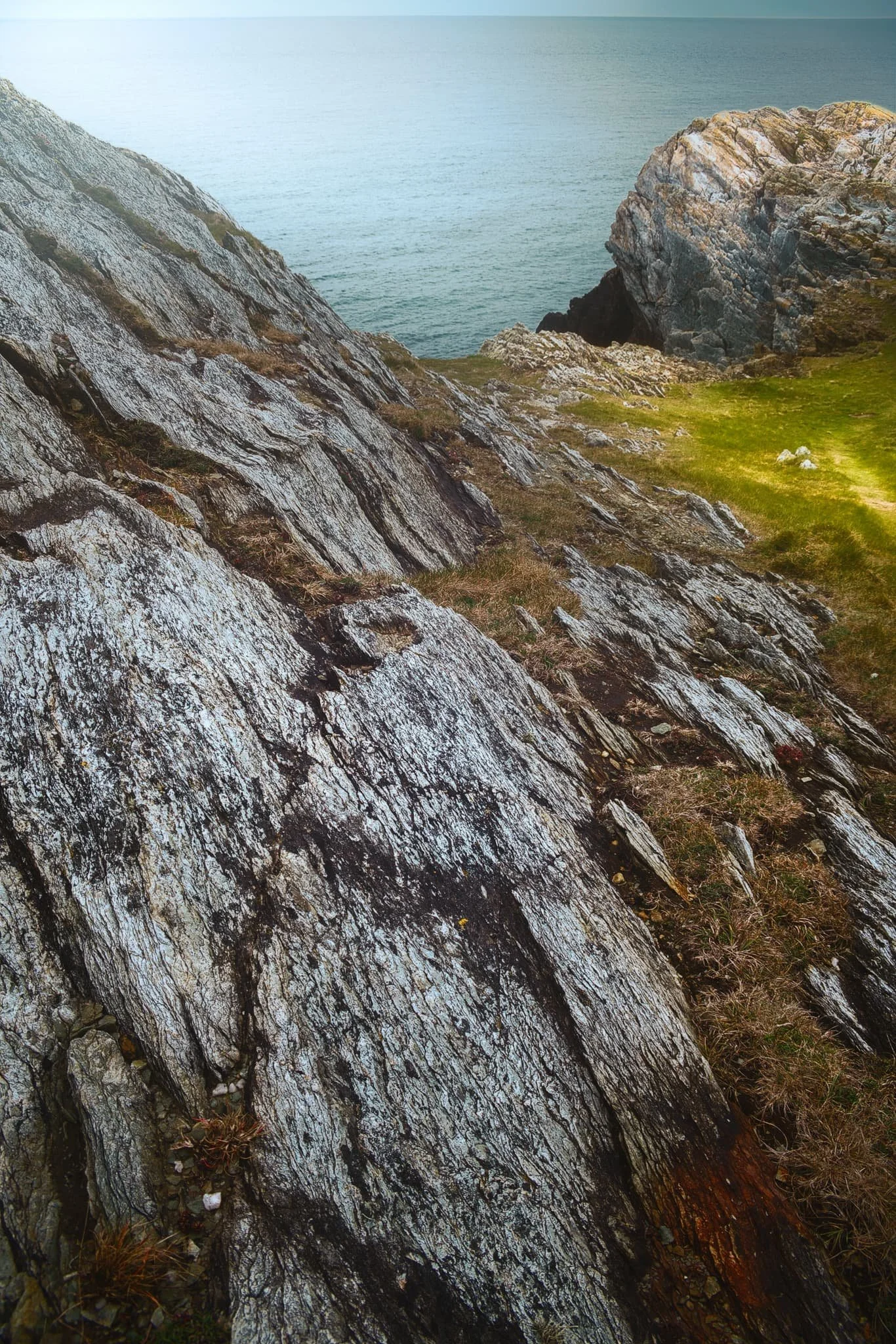  Fascinating shards of rock like plates of armour line this cliff as a strand of light escapes the thick cloud cover. 