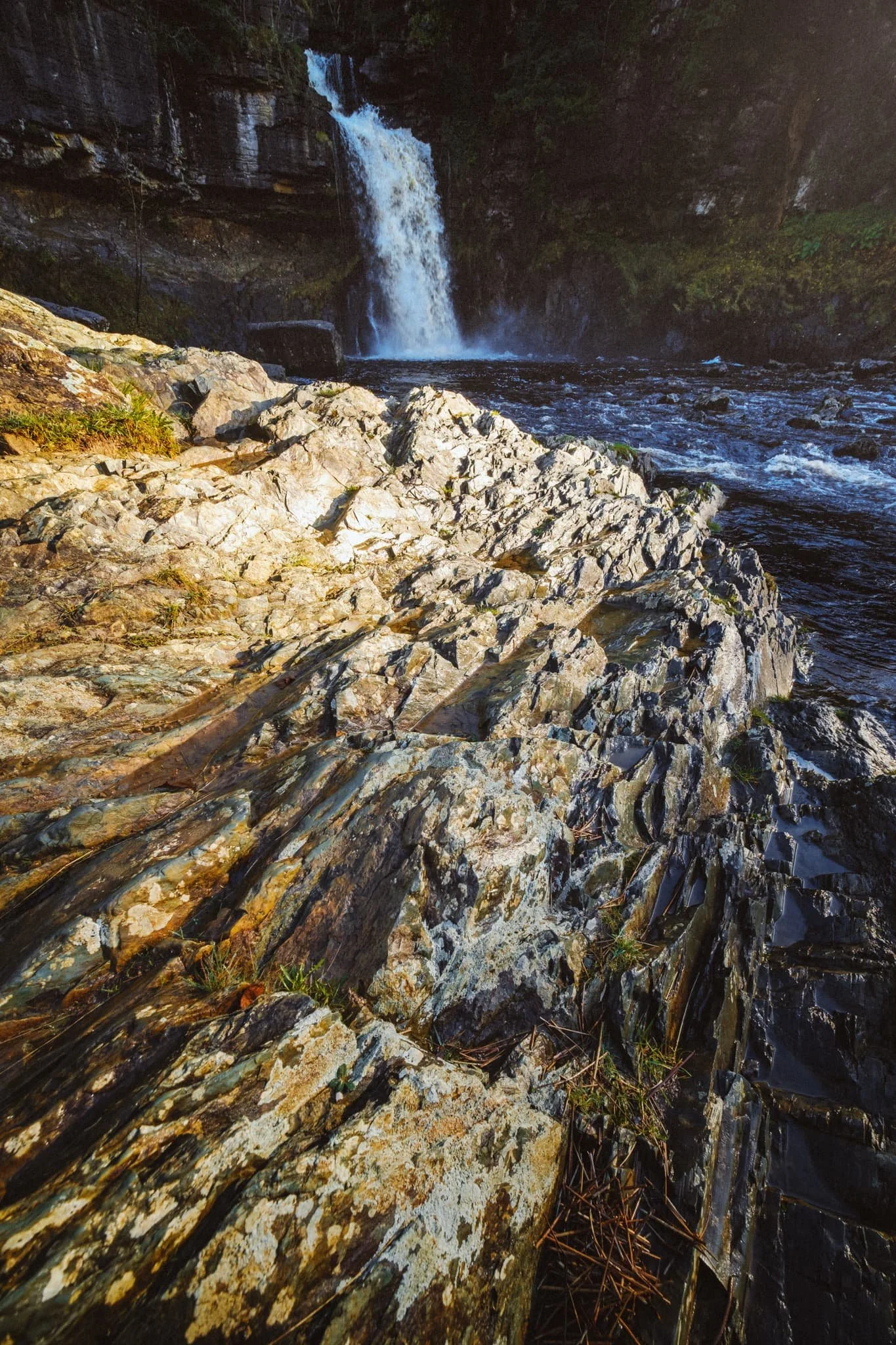  As they chat, I clamber down to the river shore and start seeking interesting compositions. Thankfully, the river bank near Thornton Force features these rock striations that I use as a leading line towards the waterfall. 