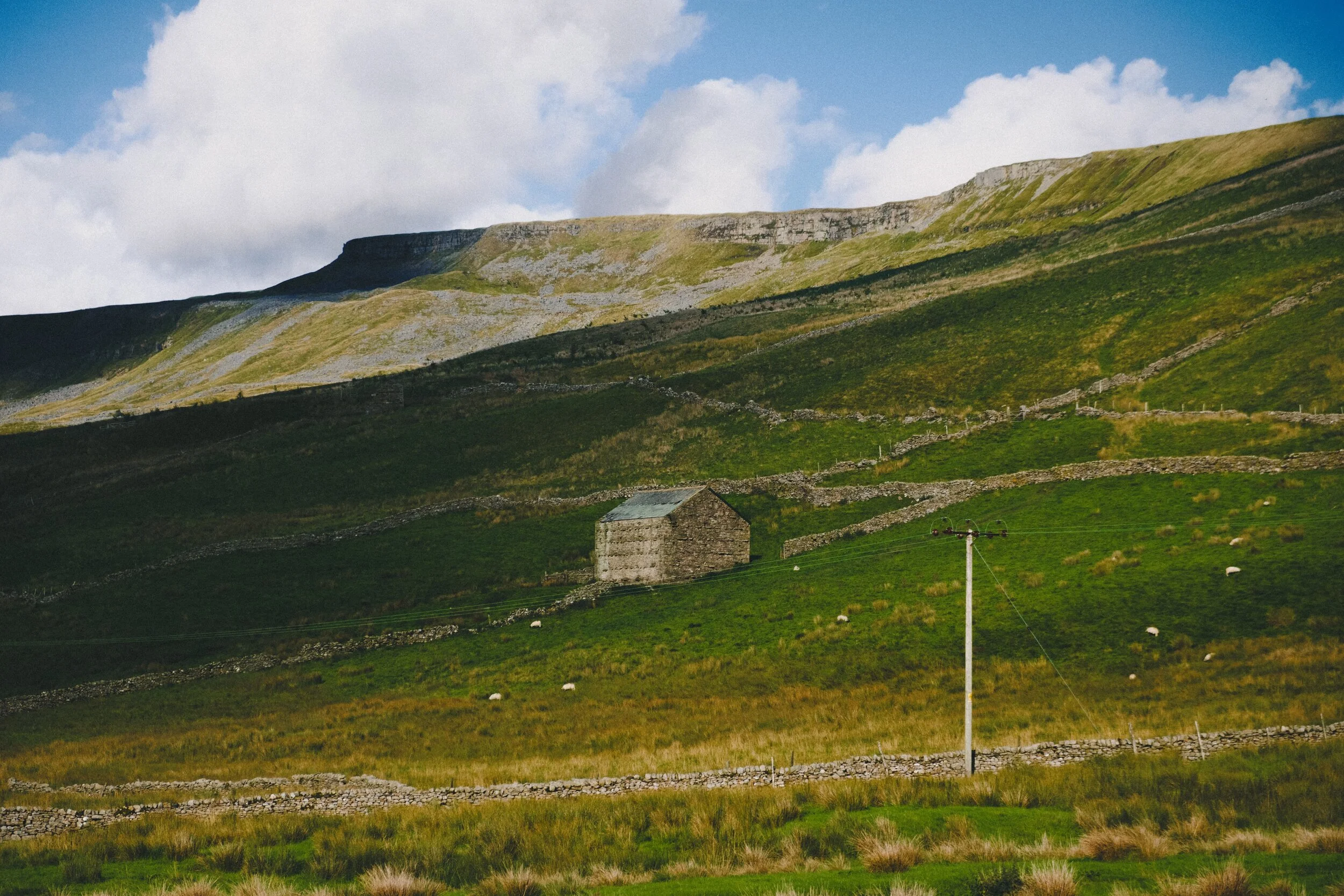 A solitary barn near Hanging Lund, below the slopes of Mallerstang Edge. Sunlight escaping from between the clouds scans across the fellside.