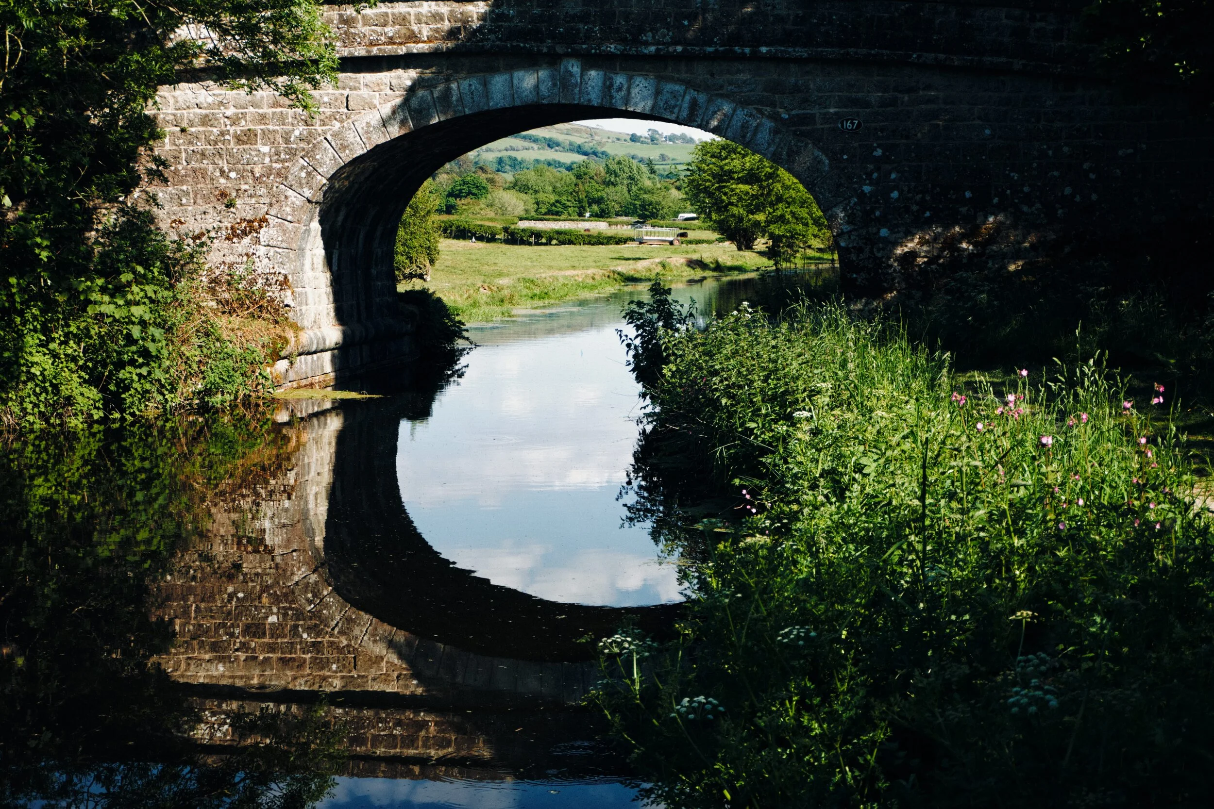 Old Hall Bridge (Nº 167) with almost perfect reflections; beyond you can just make out the slopes of Scout Hill (284 m/931 ft). On the banks before this bridge Lisabet and I were enthralled by a grey heron ( Ardea cinerea ), fishing in the waters of Lancaster Canal.