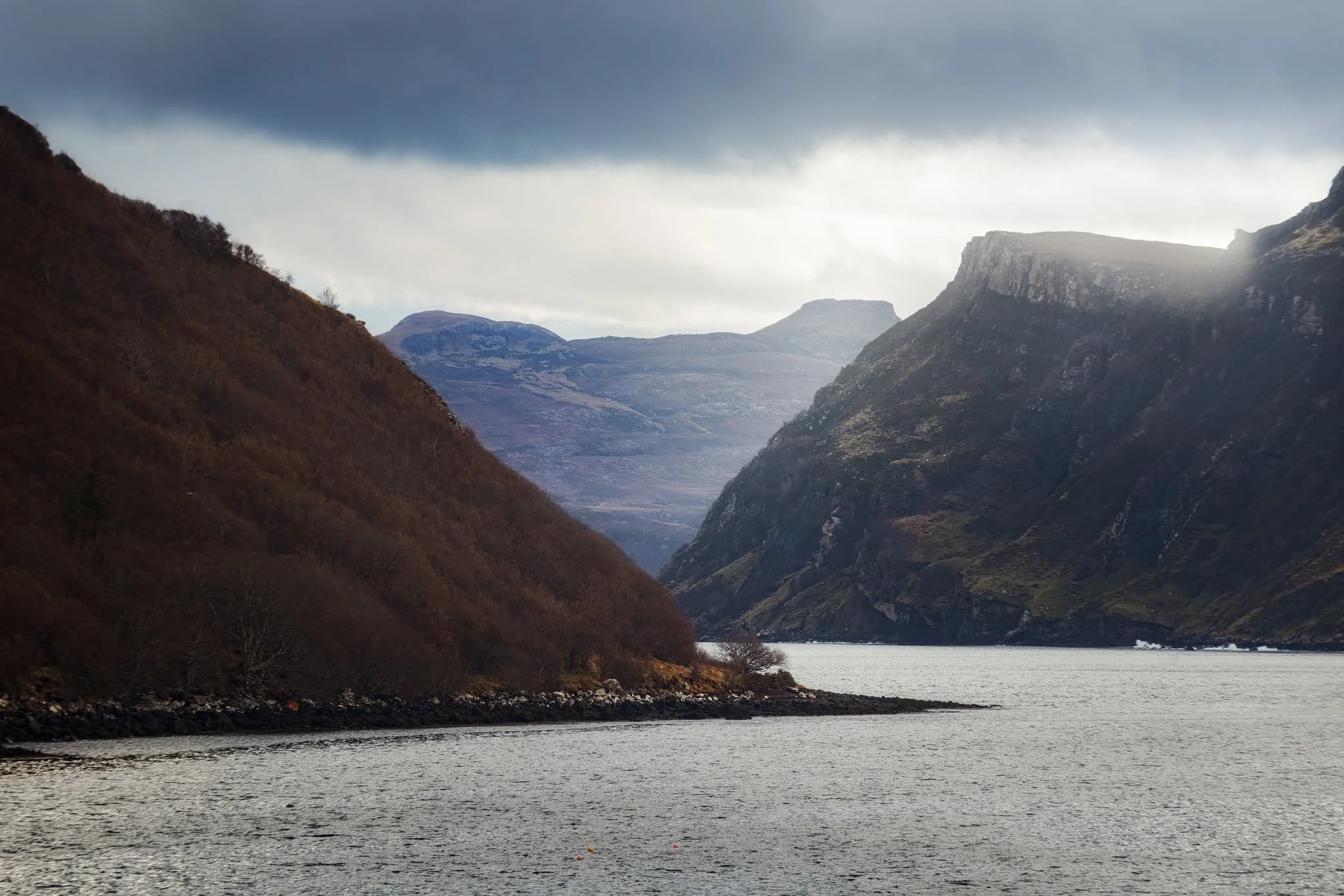  Our goal was to follow the coastal path below the left hill. But before we could get on that, this scene opened in front of me, putting me in mind of the fjords of Norway. I zoomed all the way to 210mm to get a real tight composition, involving the flanks of Ben Chracaig to the left, the crags of Ben Tianavaig to the right, and the hills of the Isle of Raasay in the middle. 