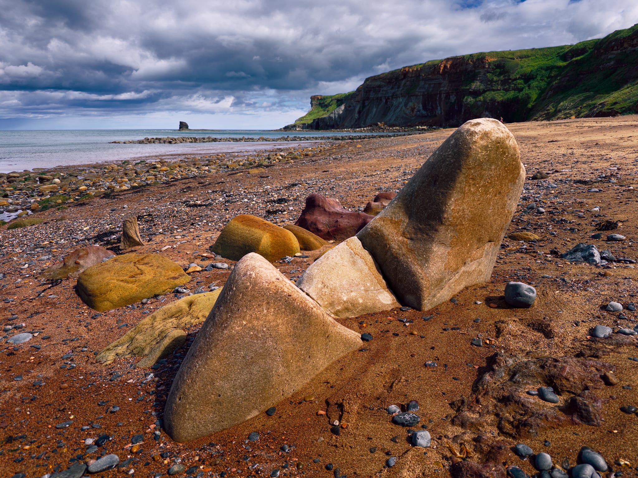 This little group fascinated me. These are sandstone blocks, fallen from the cliff and then tilted upright by wave action digging sand from underneath as the tide moves them. The wedge shapes come from the rock&rsquo;s natural jointing, they fracture along those planes when they break off the cliff face.