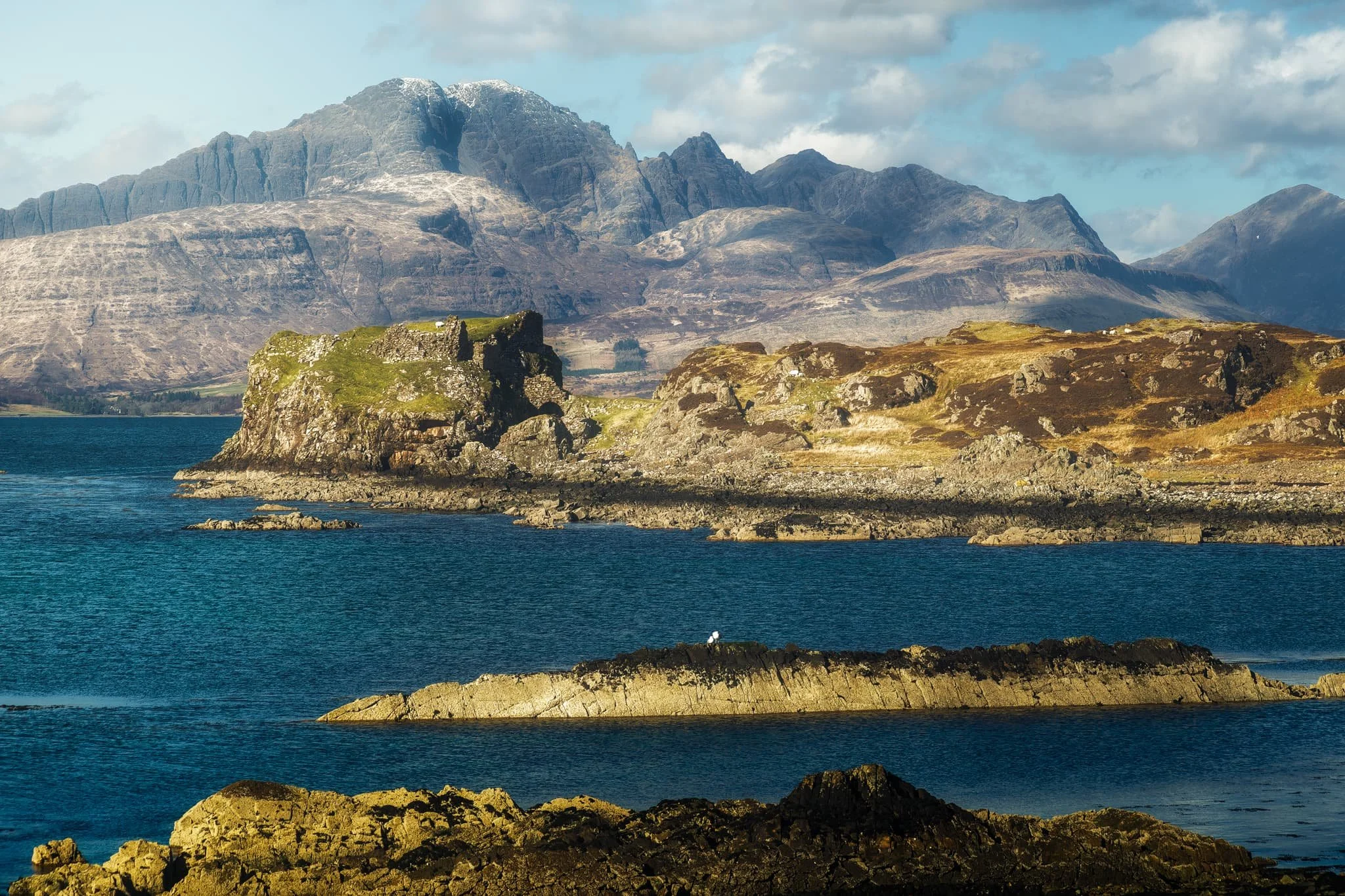  Moving on from Tarskavaig, we continue up the northern shore of Sleat to Tokavaig. At Tokavaig Bay, one can find the ruins of  Dùn Scaich  castle, formerly owned by Clan MacDonald of Sleat, a branch of the Clan Donald or MacDonald. With my long zoom lens, I can really compress the distant views, capturing the ruins of the castle as well as the mighty  Blàbheinn  mountain in the distance. 