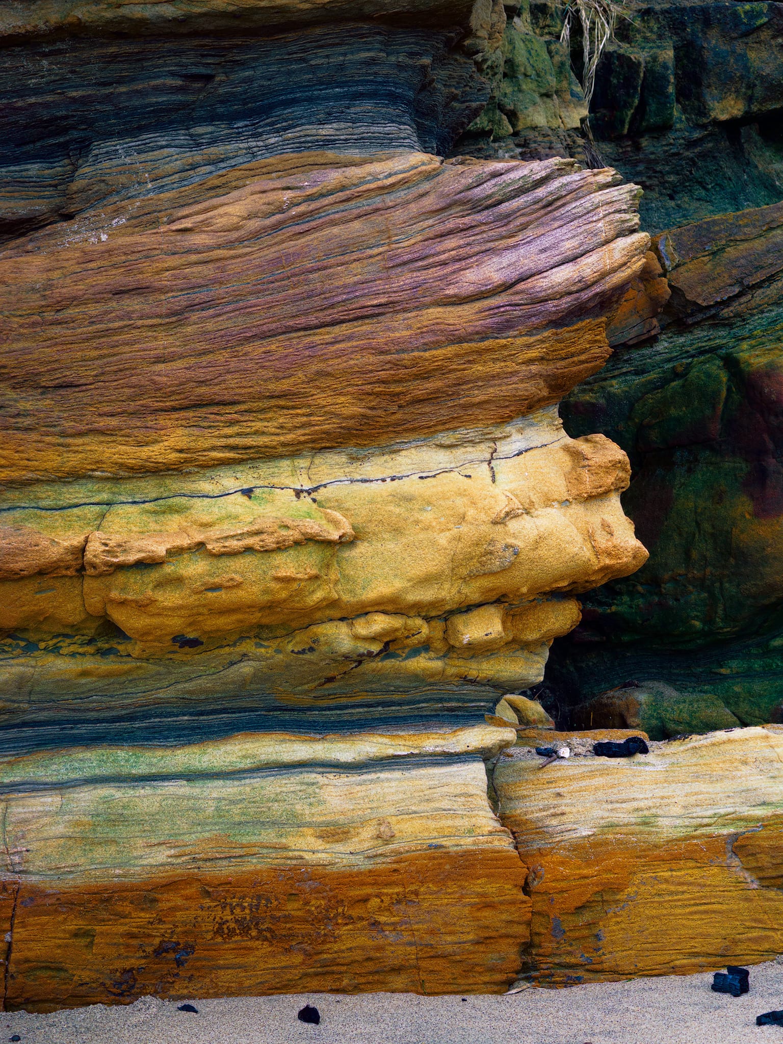 A sandwich of millions of years of history. Red beds bleached to cream, ochre, and gold by shifting groundwater chemistry, these Carboniferous cliff strata are 300 million years of delta cycles laid bare by the sea&rsquo;s relentless undermining of the softer beds below.