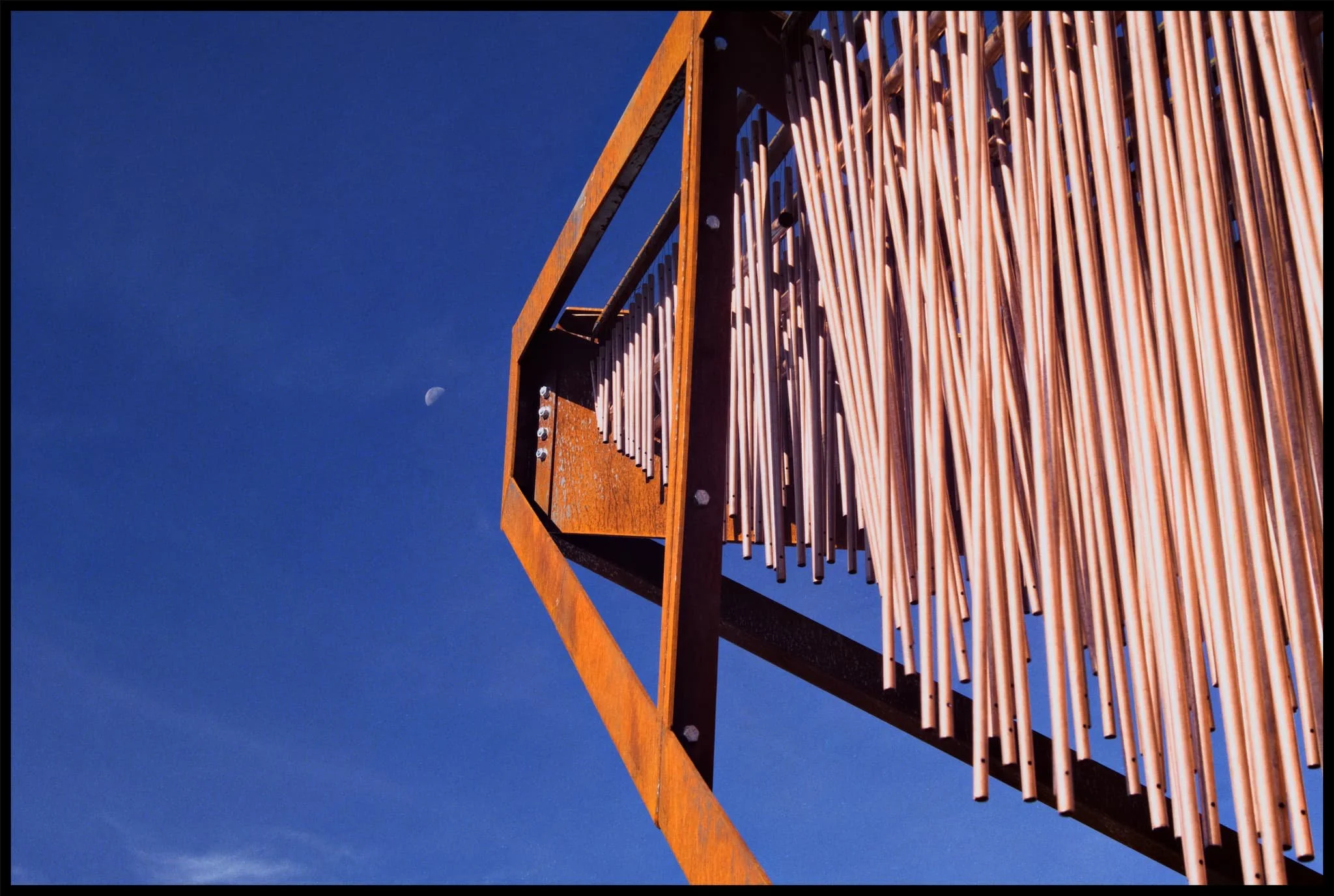  Whilst prowling around the art installation, enjoying its tones and construction, I noticed the moon was bright in the sky. I re-equipped my Vivitar and zoomed in tight to make the installation &ldquo;point&rdquo; towards the moon. 