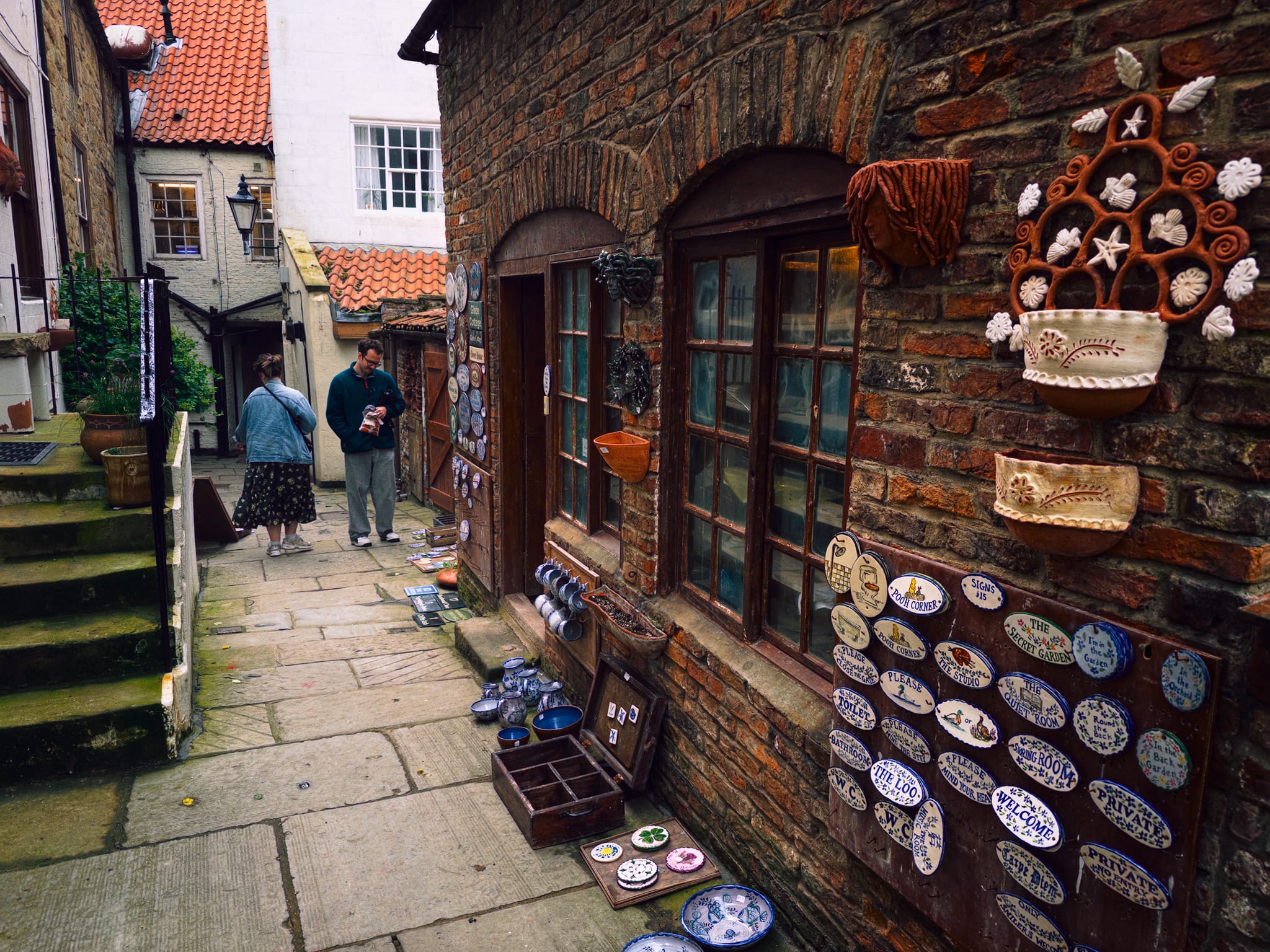 Making our way through the old town, Lisabet wanted to take a small diversion to this pottery found down a little ginnel. This is the Washouse Pottery. Laureen Shaw, an Arizonan who settled in Whitby via her grandmother, opened the pottery in 1982 in a former wash house off Church Street. It&rsquo;s now the town&rsquo;s oldest surviving pottery.
A ceramics graduate, she pivoted from gallery work to hand-painted tiles after failing to find suitable ones for her own kitchen. Her tiles and commemorative plaques blend Native American and Mexican motifs with British subjects.